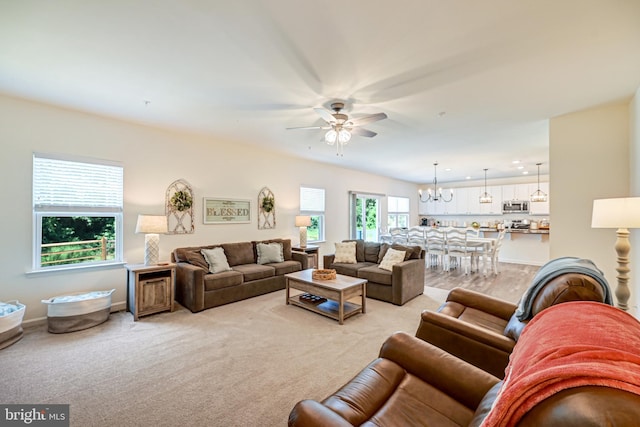 living room featuring light carpet, baseboards, and ceiling fan with notable chandelier