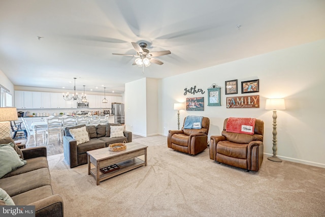 living area featuring ceiling fan with notable chandelier, baseboards, and light colored carpet