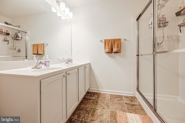 full bathroom with a sink, a tile shower, baseboards, and double vanity