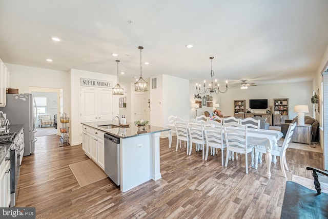 kitchen with a center island with sink, appliances with stainless steel finishes, open floor plan, wood finished floors, and white cabinetry