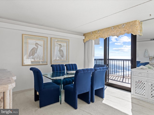 dining space with a water view, baseboards, and light colored carpet