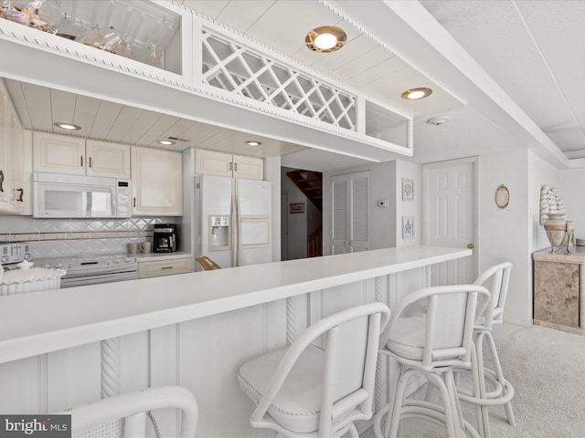 kitchen featuring carpet floors, light countertops, white cabinets, white appliances, and a kitchen bar