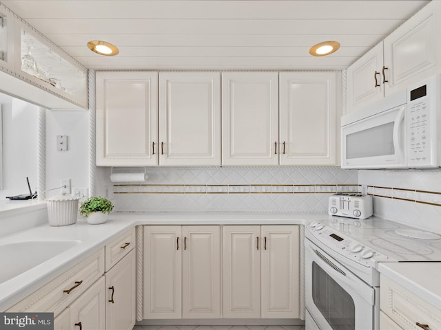 kitchen featuring light countertops, backsplash, white cabinetry, a sink, and white appliances