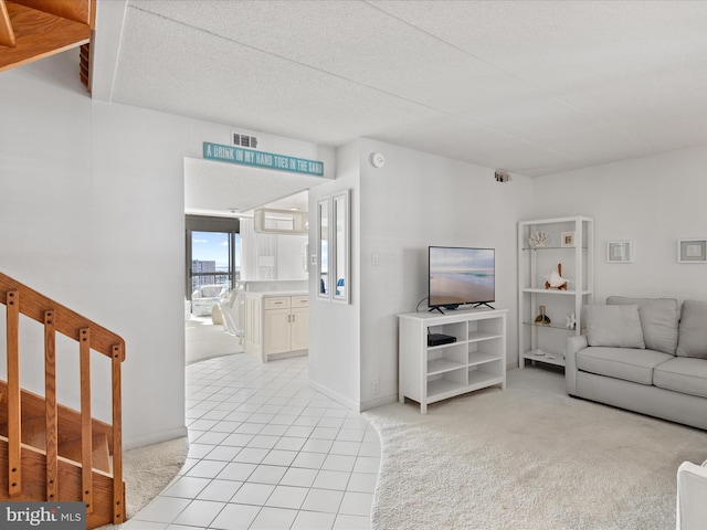 living area featuring visible vents, light colored carpet, a textured ceiling, and light tile patterned floors