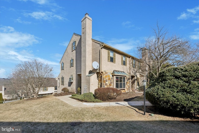 view of side of property featuring stone siding, a lawn, stucco siding, a standing seam roof, and a chimney