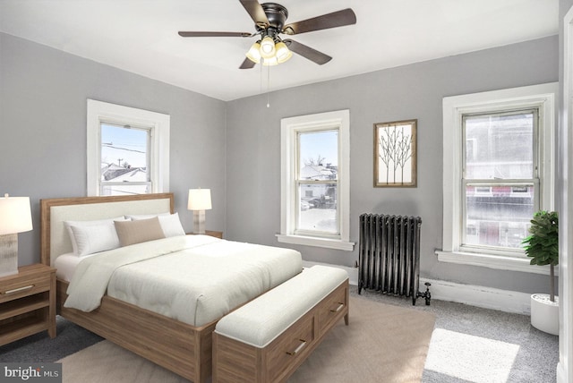 bedroom with a ceiling fan, radiator, light colored carpet, and baseboards