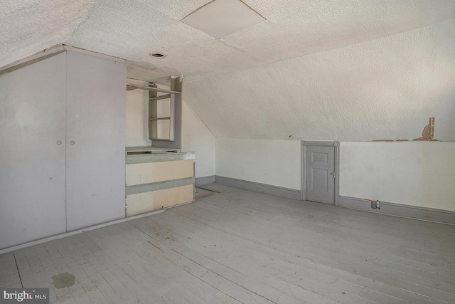 bonus room with a textured ceiling, hardwood / wood-style flooring, and vaulted ceiling