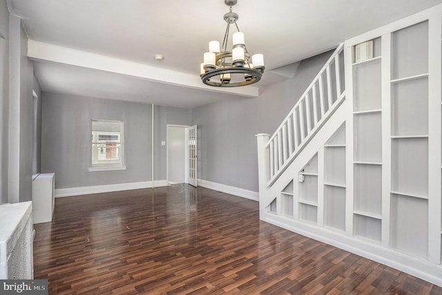 unfurnished living room with baseboards, stairs, an inviting chandelier, and wood finished floors