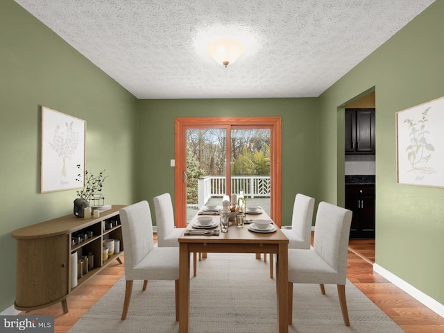 dining room featuring light wood-style flooring, baseboards, and a textured ceiling