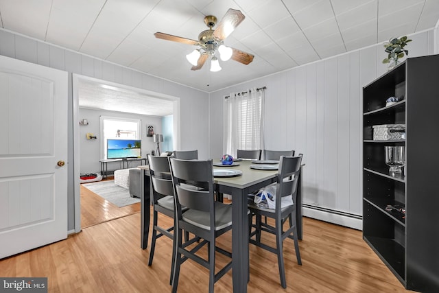 dining area featuring light wood finished floors, a baseboard heating unit, and a ceiling fan