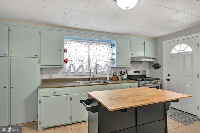 kitchen with stainless steel gas stove, butcher block counters, a kitchen island, under cabinet range hood, and a sink