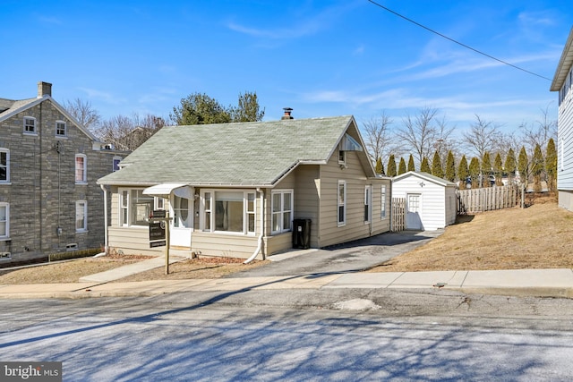 view of front of house with a shingled roof, aphalt driveway, fence, an outdoor structure, and a shed