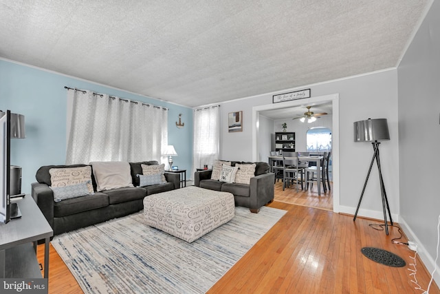 living room featuring crown molding, a textured ceiling, baseboards, and wood finished floors