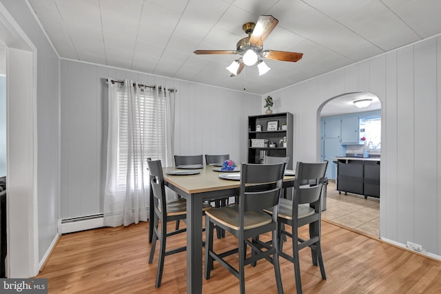 dining area featuring arched walkways, ceiling fan, light wood finished floors, and a baseboard radiator