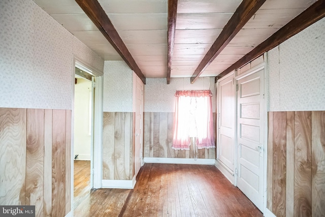 spare room with a wainscoted wall, beamed ceiling, wood finished floors, and wallpapered walls