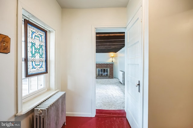 corridor featuring radiator heating unit, dark carpet, and baseboards