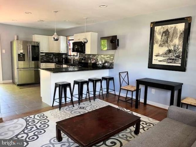 kitchen with hanging light fixtures, white cabinets, decorative backsplash, stainless steel fridge with ice dispenser, and kitchen peninsula