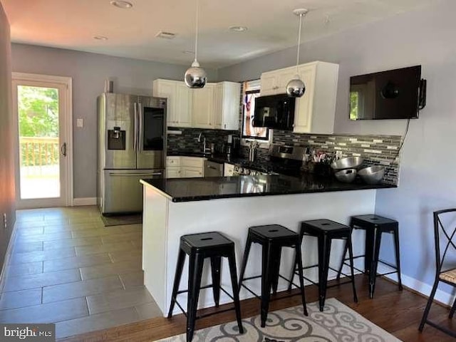 kitchen with kitchen peninsula, tasteful backsplash, appliances with stainless steel finishes, a kitchen breakfast bar, and pendant lighting