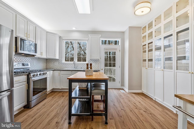 kitchen with a sink, light wood finished floors, stainless steel appliances, and decorative backsplash