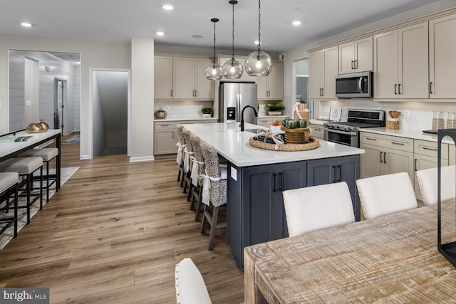 kitchen featuring appliances with stainless steel finishes, gray cabinets, hanging light fixtures, and an island with sink