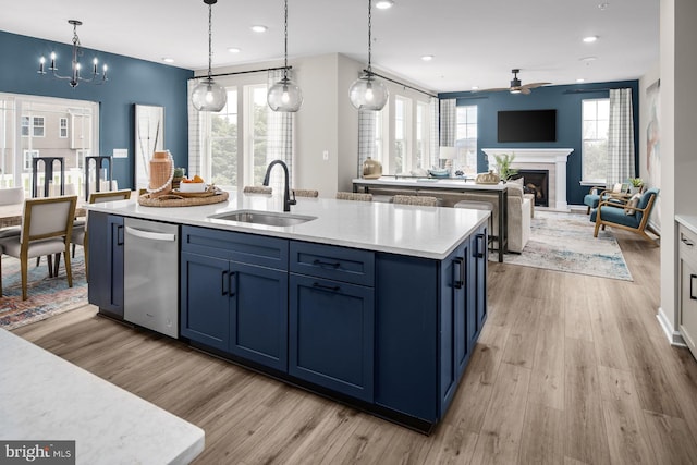 kitchen with blue cabinetry, a kitchen island with sink, sink, stainless steel dishwasher, and pendant lighting