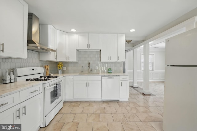 kitchen featuring tasteful backsplash, wall chimney exhaust hood, a sink, white appliances, and white cabinetry
