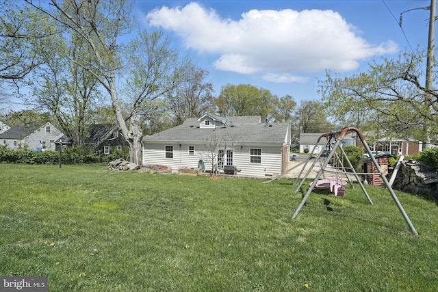 back of property with a shingled roof, a playground, and a lawn