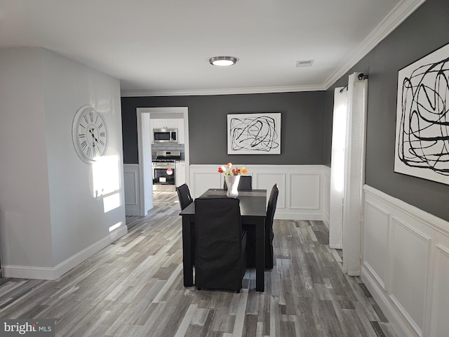 dining space with a decorative wall, wood finished floors, visible vents, and crown molding