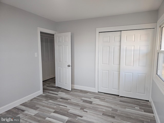 unfurnished bedroom featuring a closet, light wood-style flooring, and baseboards