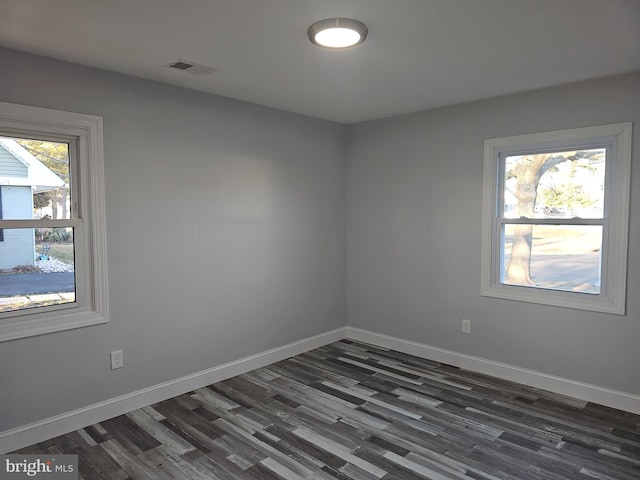 empty room featuring baseboards, visible vents, dark wood-style flooring, and a wealth of natural light