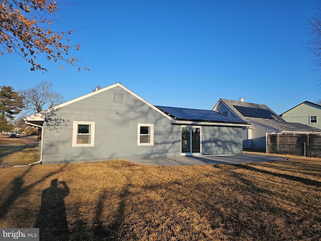 rear view of house with a patio, a lawn, fence, and roof mounted solar panels