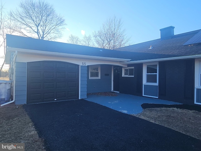 exterior space with aphalt driveway, roof with shingles, and a garage