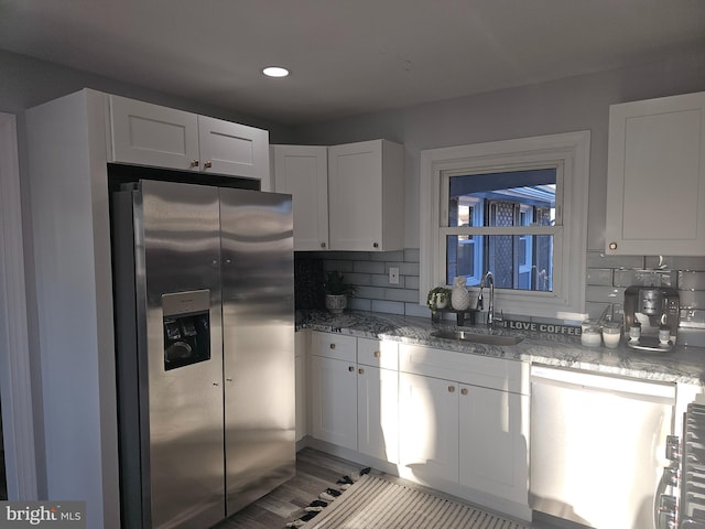 kitchen with tasteful backsplash, light stone countertops, stainless steel appliances, white cabinetry, and a sink