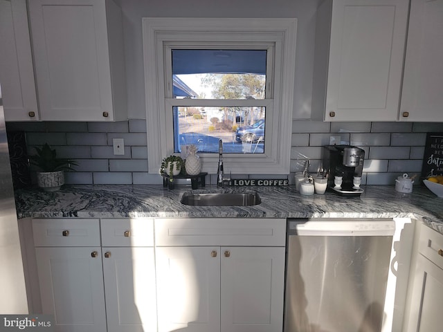 kitchen with dark stone counters, dishwasher, backsplash, white cabinetry, and a sink