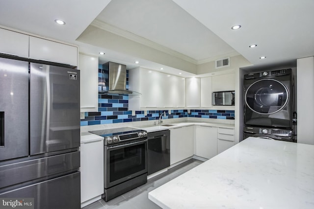 kitchen featuring visible vents, stainless steel appliances, white cabinets, stacked washer and clothes dryer, and wall chimney exhaust hood