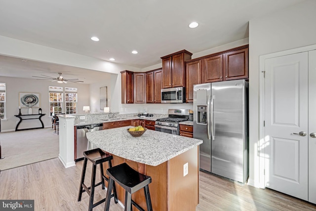 kitchen with appliances with stainless steel finishes, sink, light hardwood / wood-style flooring, a kitchen breakfast bar, and kitchen peninsula