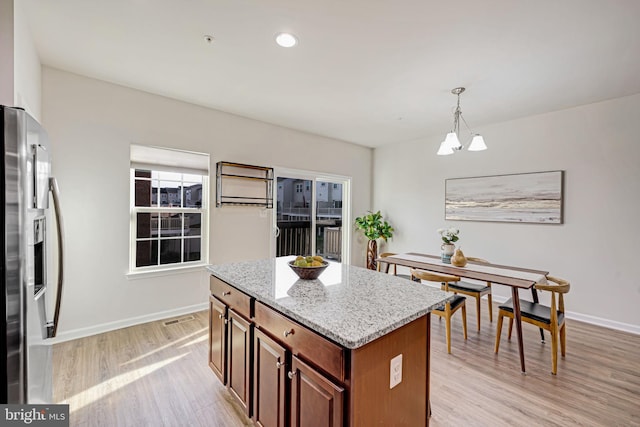 kitchen featuring stainless steel refrigerator with ice dispenser, light stone counters, a center island, pendant lighting, and light wood-type flooring