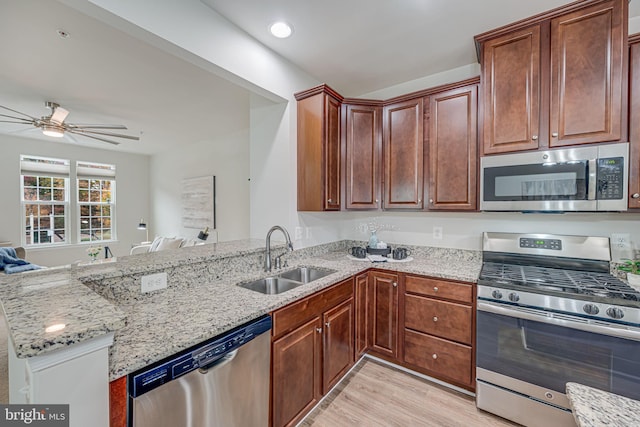 kitchen with kitchen peninsula, stainless steel appliances, light stone countertops, and sink