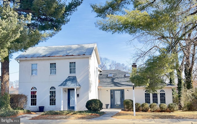 view of front of house with metal roof, a chimney, and stucco siding