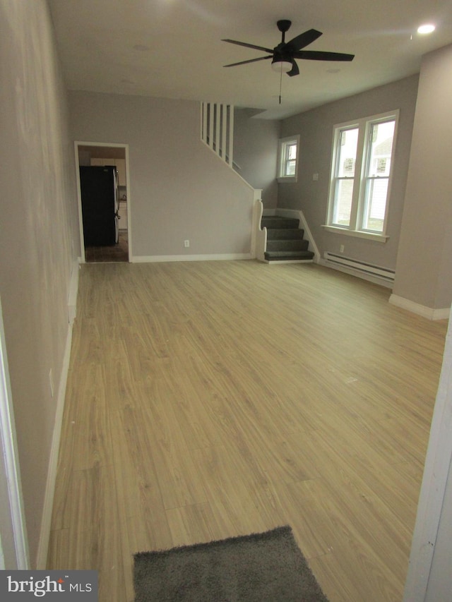 unfurnished living room featuring light wood finished floors, baseboards, a ceiling fan, stairs, and baseboard heating