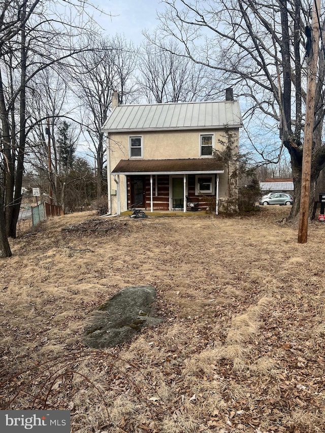 view of front of home with metal roof, a porch, stucco siding, a standing seam roof, and a chimney