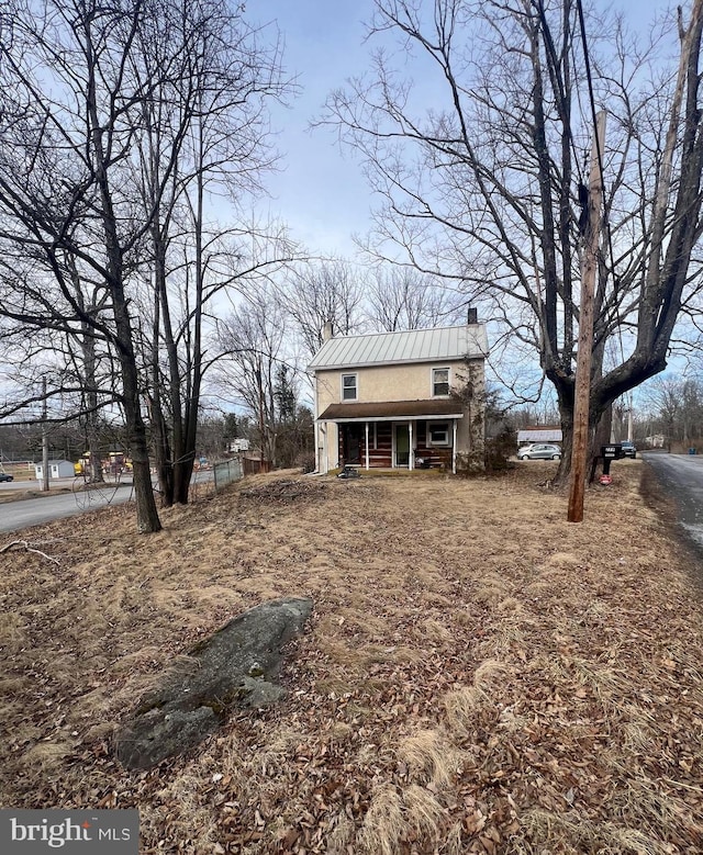 exterior space featuring a standing seam roof, a chimney, metal roof, and covered porch