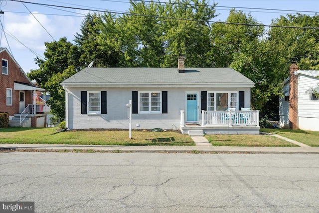 view of front of property featuring a front yard, brick siding, covered porch, and a chimney