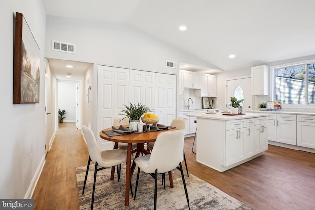 dining room with high vaulted ceiling, wood-type flooring, and sink