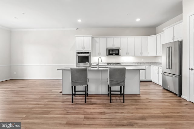 kitchen with appliances with stainless steel finishes, a breakfast bar, white cabinetry, light hardwood / wood-style floors, and an island with sink