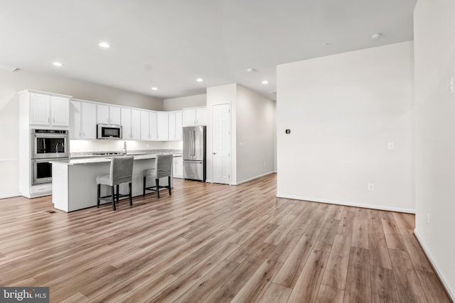 kitchen featuring a kitchen island with sink, light hardwood / wood-style flooring, appliances with stainless steel finishes, white cabinets, and a breakfast bar area