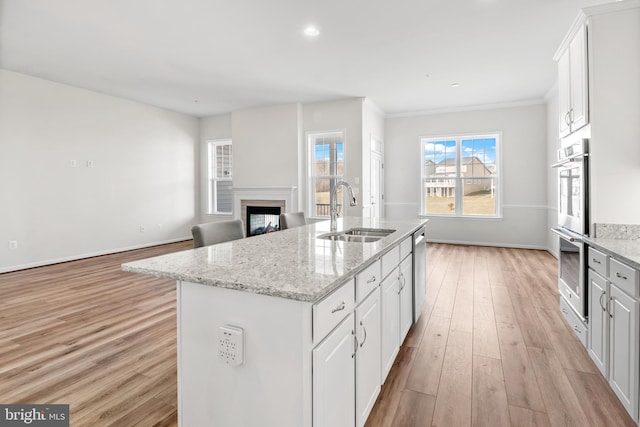 kitchen featuring light wood-type flooring, an island with sink, light stone countertops, sink, and white cabinetry