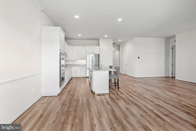 kitchen with an island with sink, white cabinetry, a kitchen breakfast bar, and light wood-type flooring