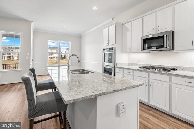 kitchen with appliances with stainless steel finishes, an island with sink, light stone counters, sink, and white cabinetry