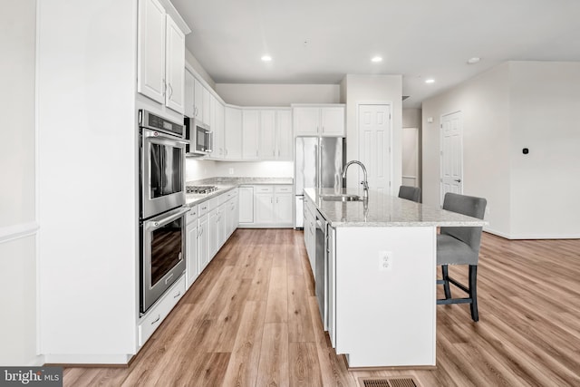 kitchen with white cabinets, stainless steel appliances, a kitchen island with sink, and sink